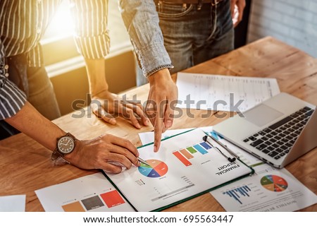 young business man hand holding pen and partner pointing graph chart for  analyze the company's sales plan in the office.