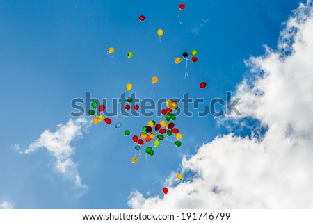 Many balloons fly into the blue sky with big clouds