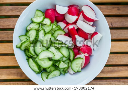 Fresh red radishes and cucumbers on a white plate, wood background