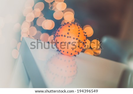 Aromatic Christmas orange with cloves with lights bokeh in background, soft focus, strong backlight