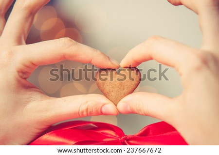 Girl Fingers Holding Hearth Shaped Gingerbread Cookie, blurred background, vintage edition