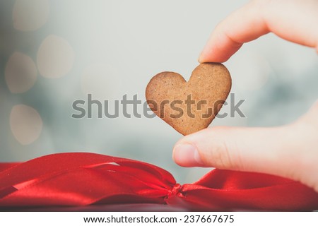 Girl Fingers Holding Hearth Shaped Gingerbread Cookie, blurred background, vintage edition
