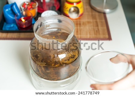 Glass teapot with blooming tea flower inside. Pour tea into a cup.