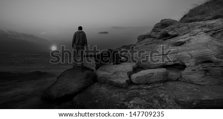 black and white sunrise seascape with alone man on the rocks
