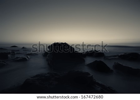 duotone sea landscape with rock and smooth water in sunrise time
