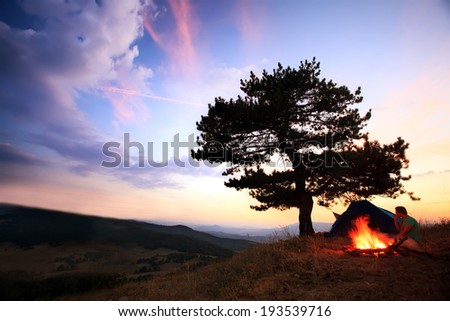 Blazing bonfire in mountain, scenic HDR camp background with two man