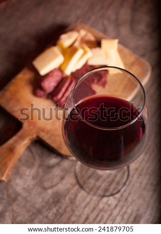 wine glass on wooden table , tasty cheese and salamy in background