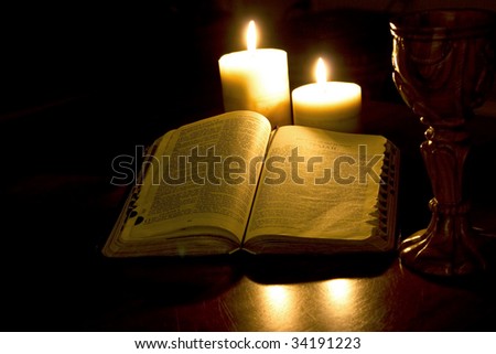 Bible open to the book of Isaiah lit by candlelight with carved chalice