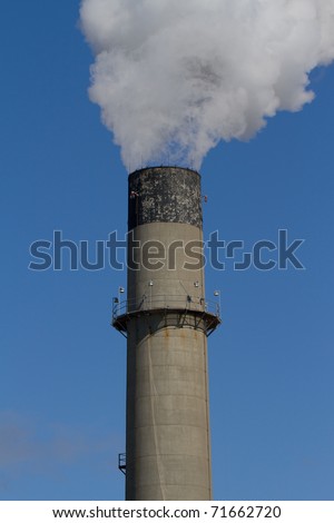 Large electrical plant smokestack pouring out plume of white smoke against blue sky
