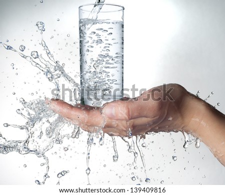 human hands with glass and water splashing on them