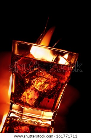cola with cognac or whiskey in glass and fire on black background