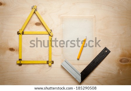 Folding rule setting up in shape of a house  on wooden background.