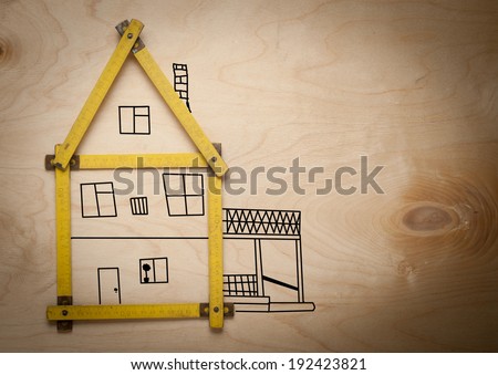 Folding rule setting up in shape of a house on wooden background. House consept.