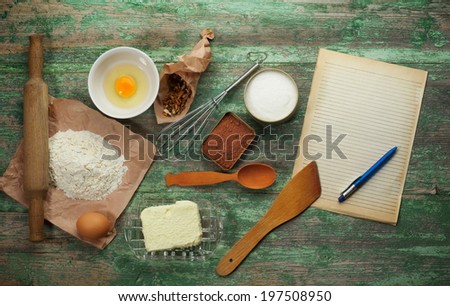 Baking cake in rural kitchen - dough recipe ingredients (eggs, flour, butter, sugar, cocoa, nuts and rolling pin on vintage wood table from above. Rustic background with free text space.