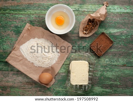 Baking cake in rural kitchen - dough recipe ingredients (eggs, flour,  butter, sugar, cocoa, nuts) on vintage wood table from above. Rustic background with free text space.