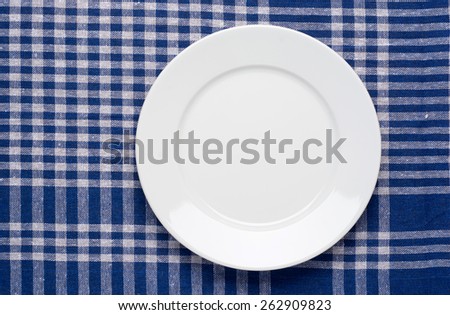 White classic plate on blue checkered tablecloth. Top View.