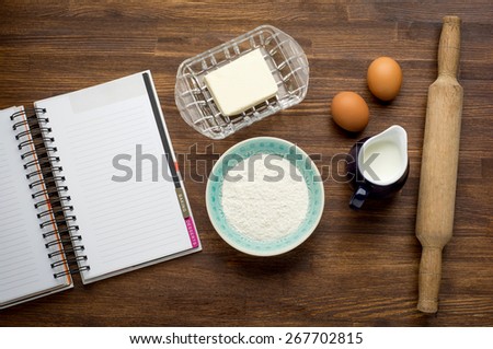 Ingredients for baking cake: eggs, flour, milk, butter on vintage wooden table with Recipe book.