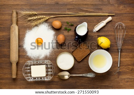 Baking cake in rural kitchen - dough recipe ingredients (eggs, flour, milk, butter, sugar) on vintage wooden table from above.