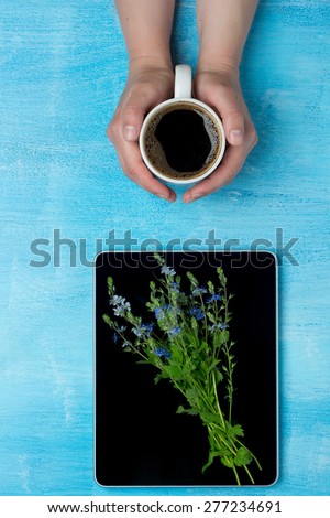 Woman holding hot cup of coffee and tablet computer with flowers on. Rendezvous concept