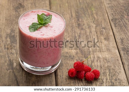 Raspberry smoothie in a glass on wooden table, up view.