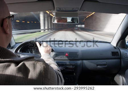 man driving a car about to enter a tunnel, shot from the backseat