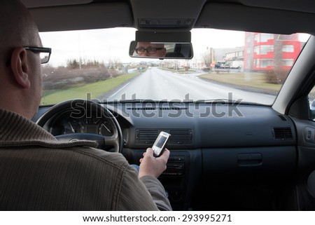 Man messaging on mobile while driving, shot from the backseat