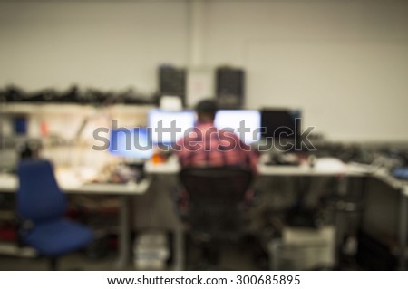 Out of focus shot of a man working in a computer repair center, computer parts and screens all around him