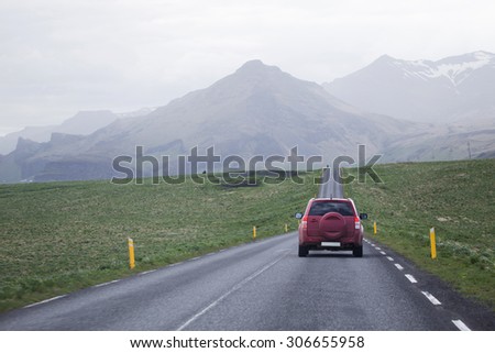 Small jeep driving on a road in rural settings towards mountains ahead.