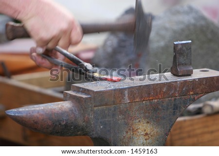A craftsman/blacksmith working metal the oldfashioned way, with hammer and anvil and open fire