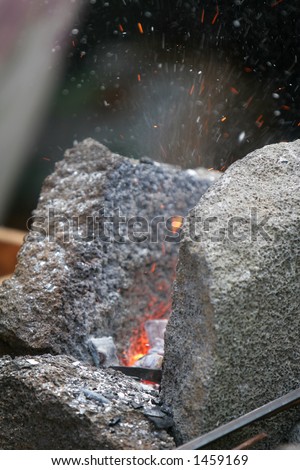 A craftsman/blacksmith working metal the oldfashioned way, with hammer and anvil and open fire, sparks flying off fireplace