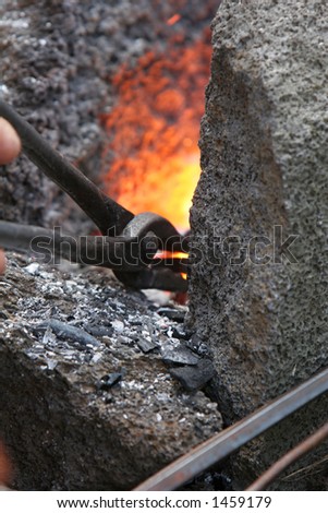 A craftsman/blacksmith working metal the oldfashioned way, with hammer and anvil and open fire, using wrench to pull metal out of fire