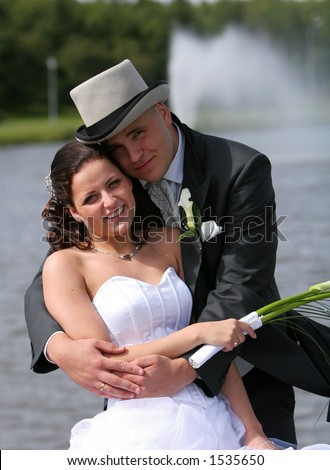 Bride and groom standing on front of water fountain, broom holding the bride and both looking at camera