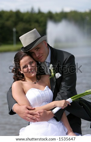 A wedding, bride and groom standing and posing for the camera in front of a fountain , which is blurry in the background