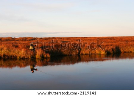 A flyfisher casting his line in a calm river in autumn