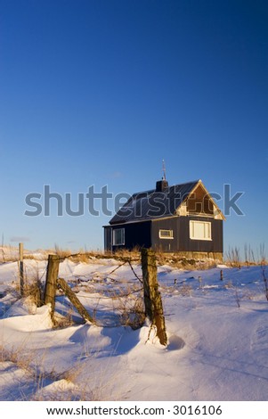 A shot of a lonely old house on a hill in winter, snow on ground and deep blue sky