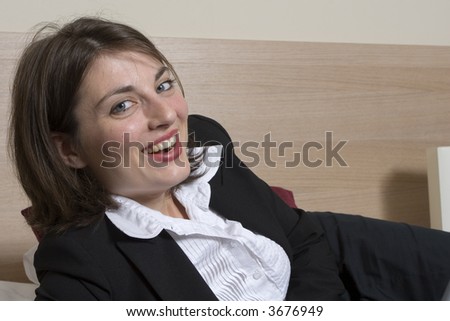beautiful, smartly dressed young woman lying on a bed typing on a laptop, smiling