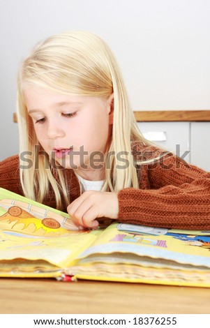 Young blond first grade girl reading a book for her homework