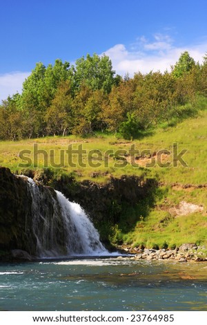 A small waterfall during summer, set against gentle hills with small trees on top of it