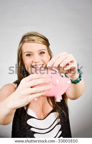 Pretty young woman smiling and putting coin into a pink piggy bank