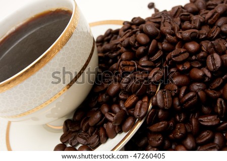 cropped shot of a fine china cup full of coffee with coffee beans all around