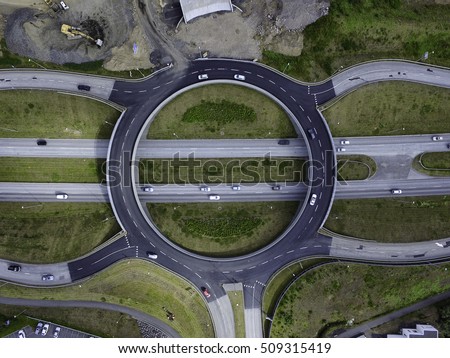 Aerial image of a roundabout over a 4 lane highway, cars on the road and road construction to the side