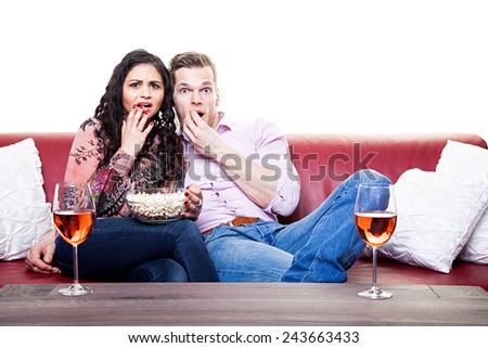 Couple watching scary movie on the sofa with bowl of popcorn at home in the living room