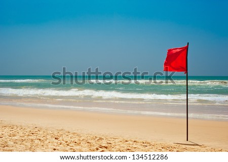 Swimming is dangerous in ocean waves. Red warning flag flapping in the wind on beach at stormy weather