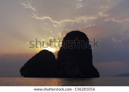 Sunset at tropical beach landscape. Ocean coast with rock formation island silhouette under evening sun. Pranang cave beach, Railay, Krabi, Thailand