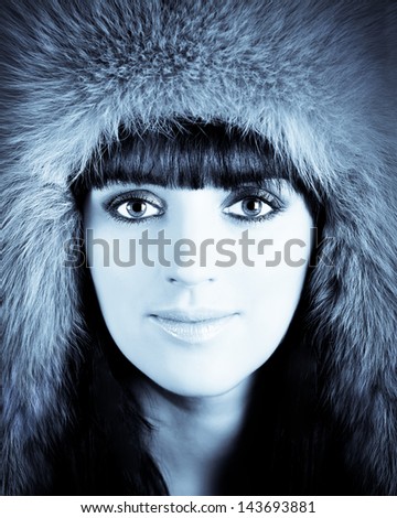 Winter portrait of young beautiful woman in furry hat with professional make up. Blue colored image, high contrast