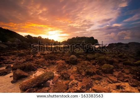 Ocean landscape of tropical beach with rocks and stones under colorful dramatic sunset sky. Cay at evening low tide. Thailand, Phuket