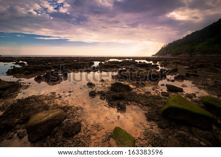 Ocean landscape of tropical beach with rocks and stones under colorful dramatic sunset sky. Cay at evening low tide. Thailand, Phuket