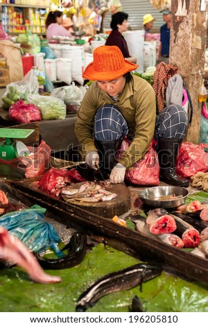 SIEM REAP, CAMBODIA - DEC 22, 2013: Unidentified Khmer woman cleaning and selling fish at food marketplace on Dec 22, 2013 in Siem Reap, Cambodia. Street food markets is popular tradition in asia