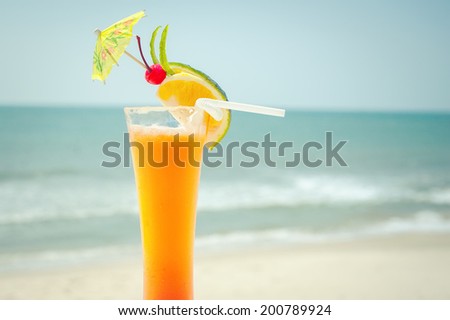 Tequila sunrise cocktail with fruits and umbrella decoration at tropical ocean beach. Vintage style, hipster colors image with copy space for party invitation text