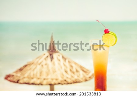 Long Island cocktail with fruits decoration at tropical ocean beach with umbrella. Vintage style, hipster colors image with copy space for party invitation text